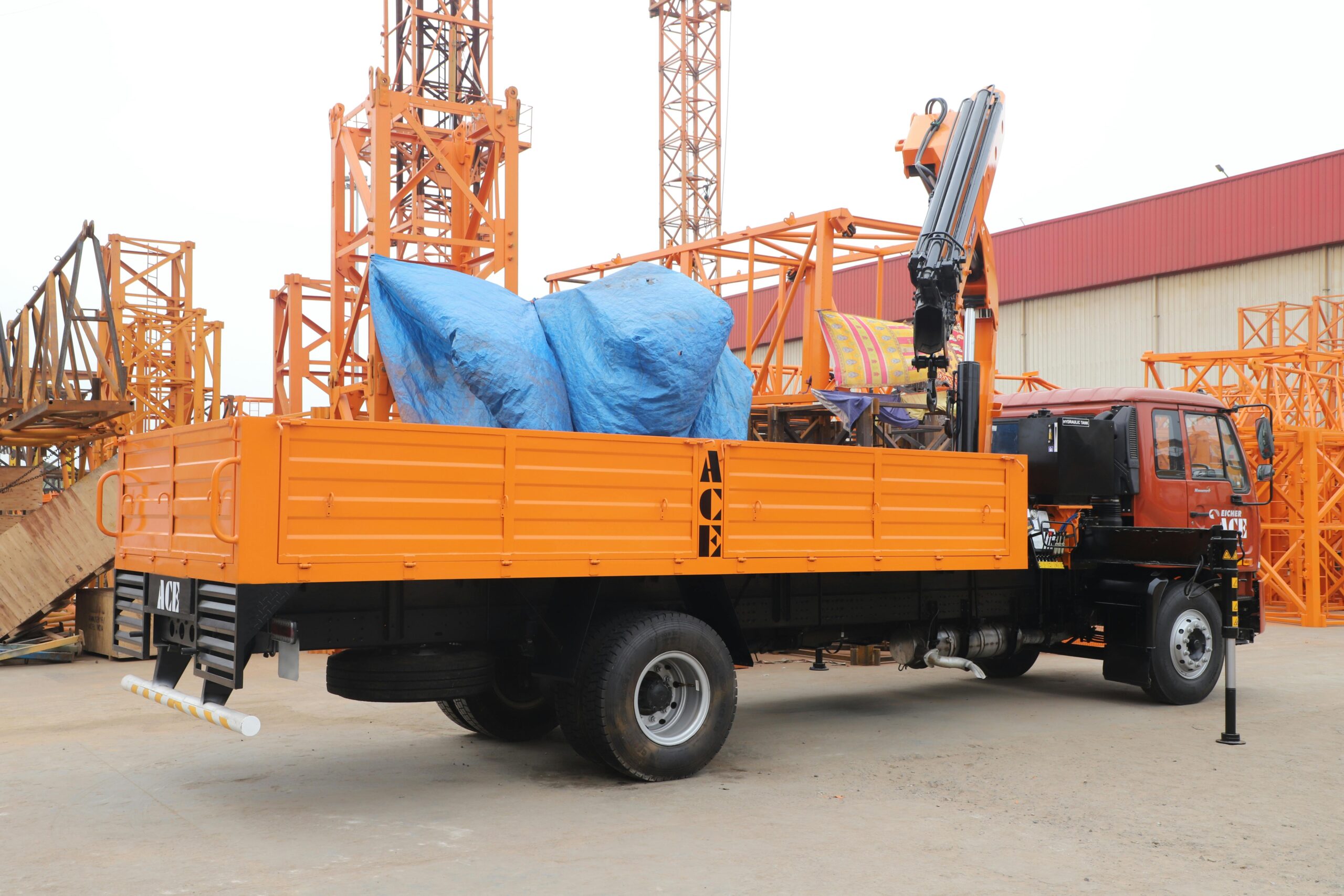 Orange truck with crane at construction site in Faridabad, India.
